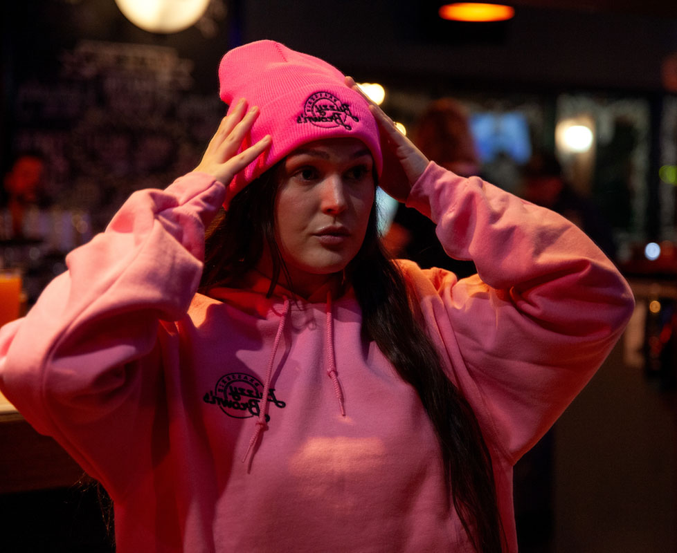 A woman wearing a pink knit Buzzy Brown's toque and hoodie.